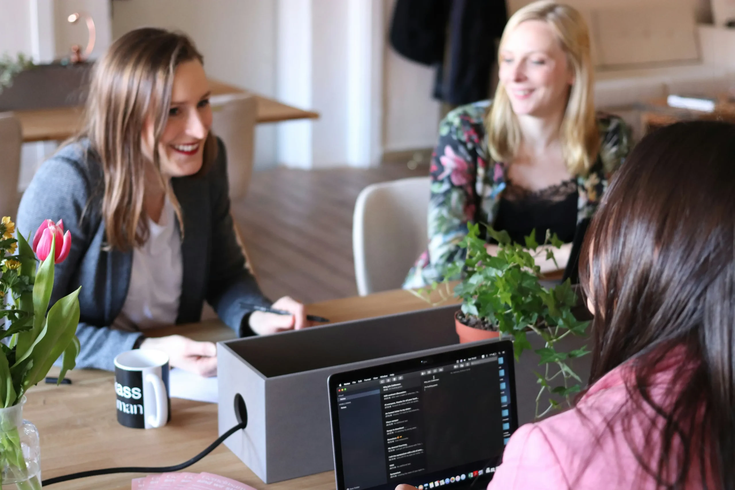 Three women at a desk with a laptop, in discussion.