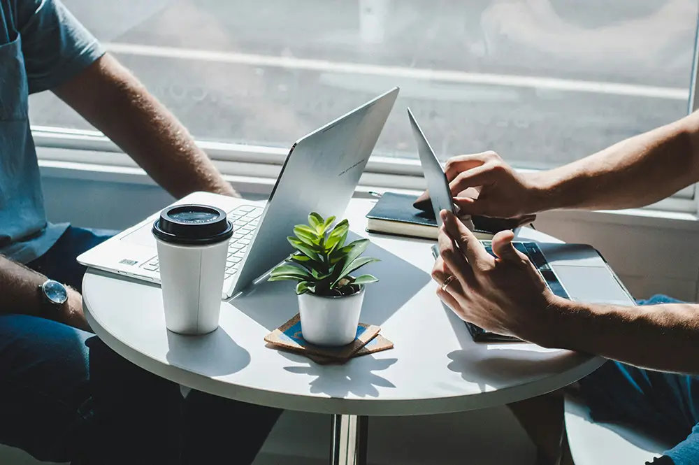 Close up of two laptops on a table, with hands in shot.
