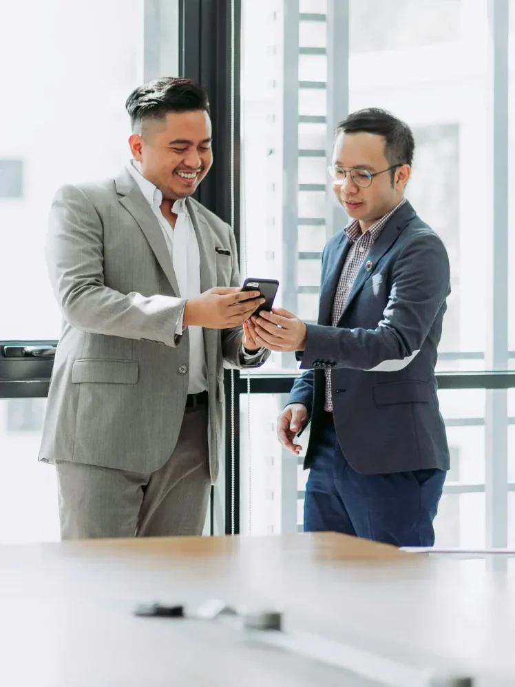 Two businessmen in an office, looking at a mobile phone.