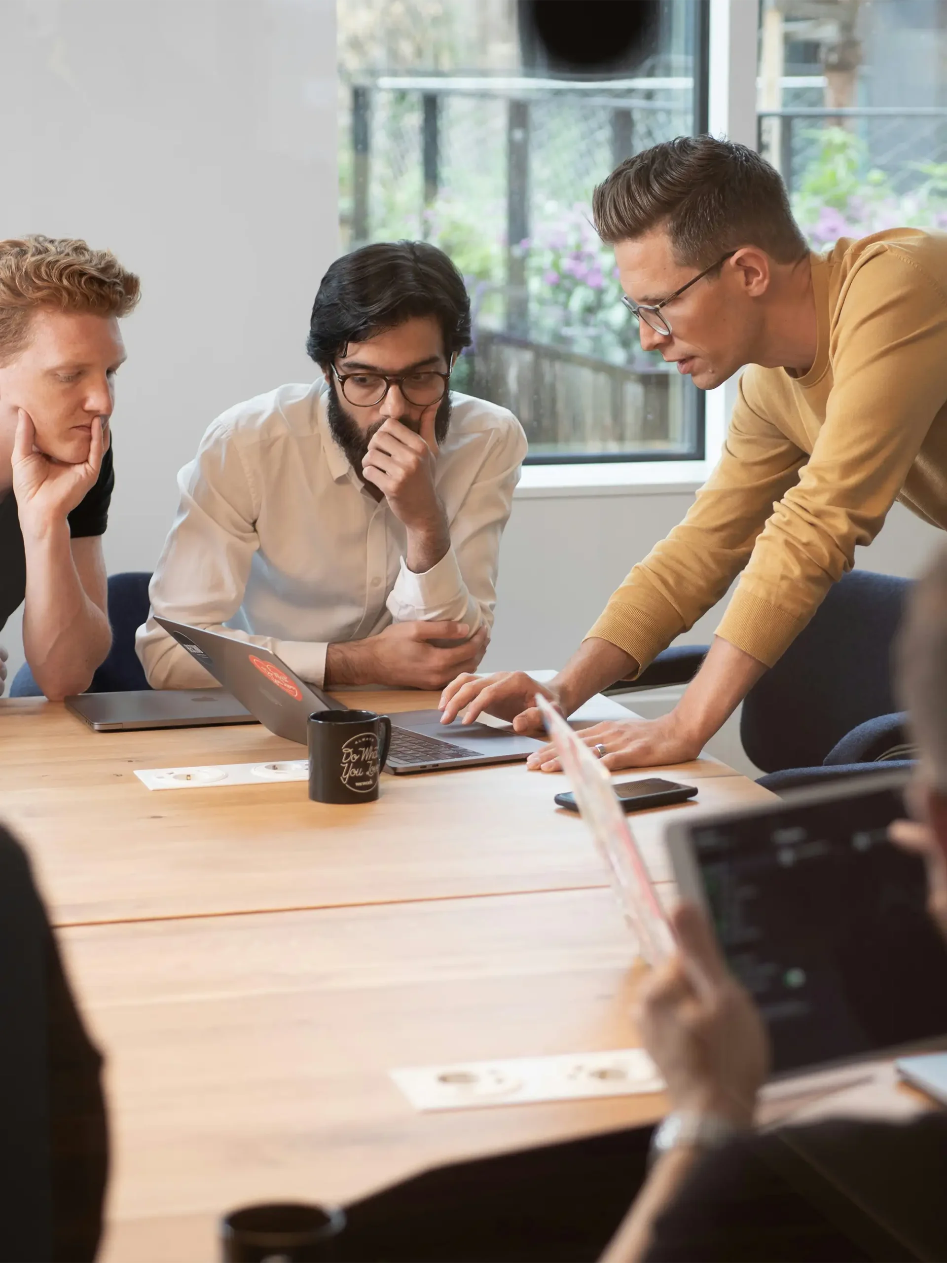 Three men in a meeting room, huddled around a laptop.