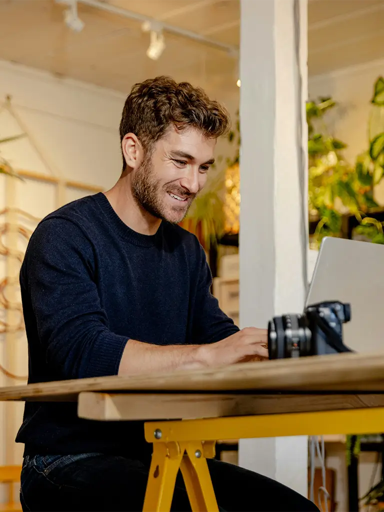 Man sat in a co-working space, smiling at a laptop.